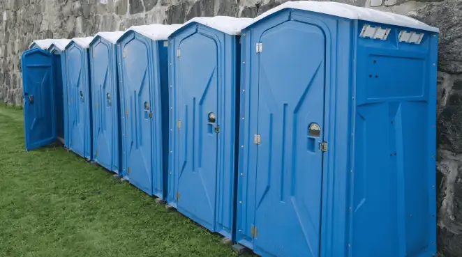 Row of blue portable toilets lined up on grass against a stone wall for event sanitation in Sarasota, FL