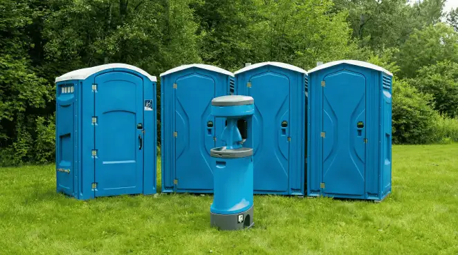 Four blue portable toilets and a matching hand washing station on grass near trees, a common sight at local outdoor events in Sarasota, FL